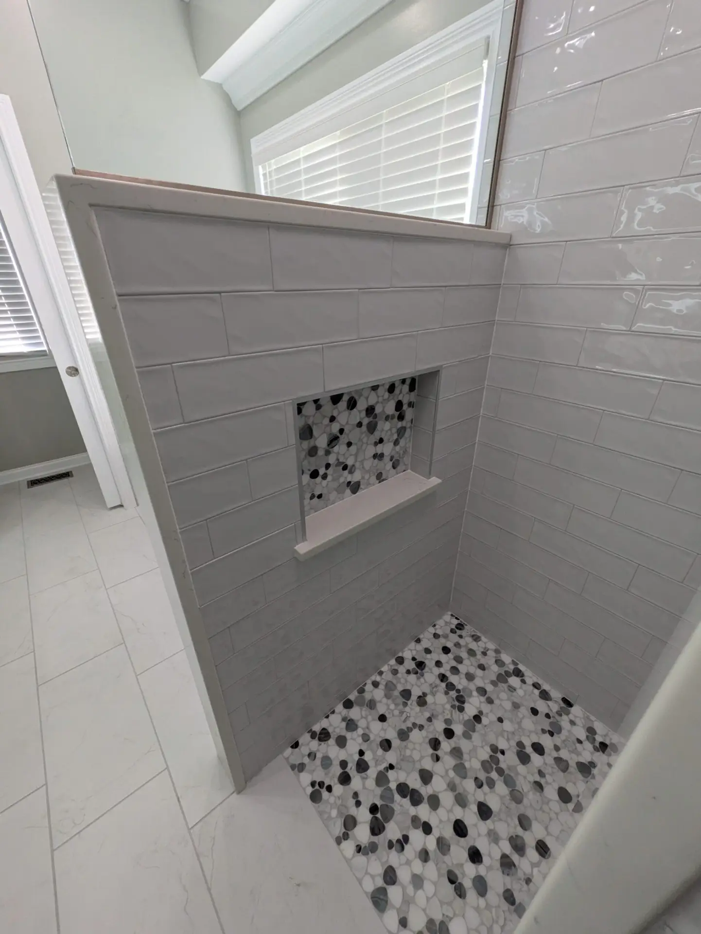 Accessible walk-in shower with white subway tile, a built-in niche and a pebble tile floor