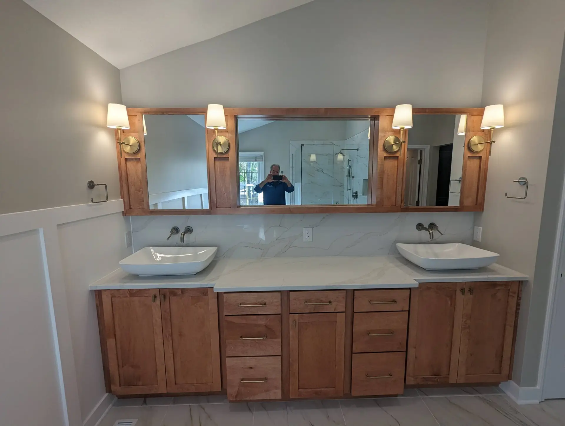 Remodeled bathroom with double vessel sinks on a wood vanity and a framed mirror with wall sconces