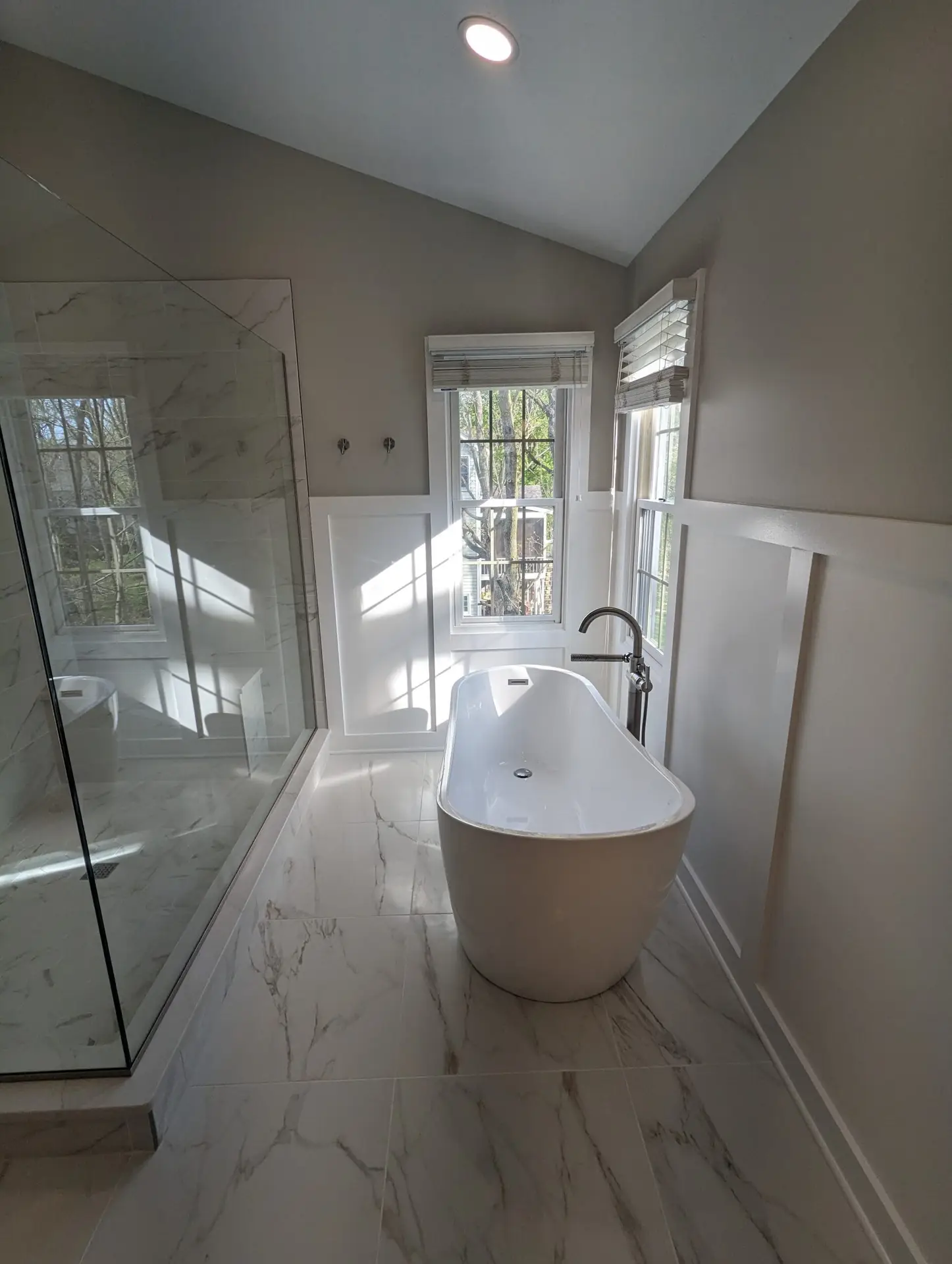 Spa-like primary bathroom with a freestanding tub, glass shower and wood-look tile floor
