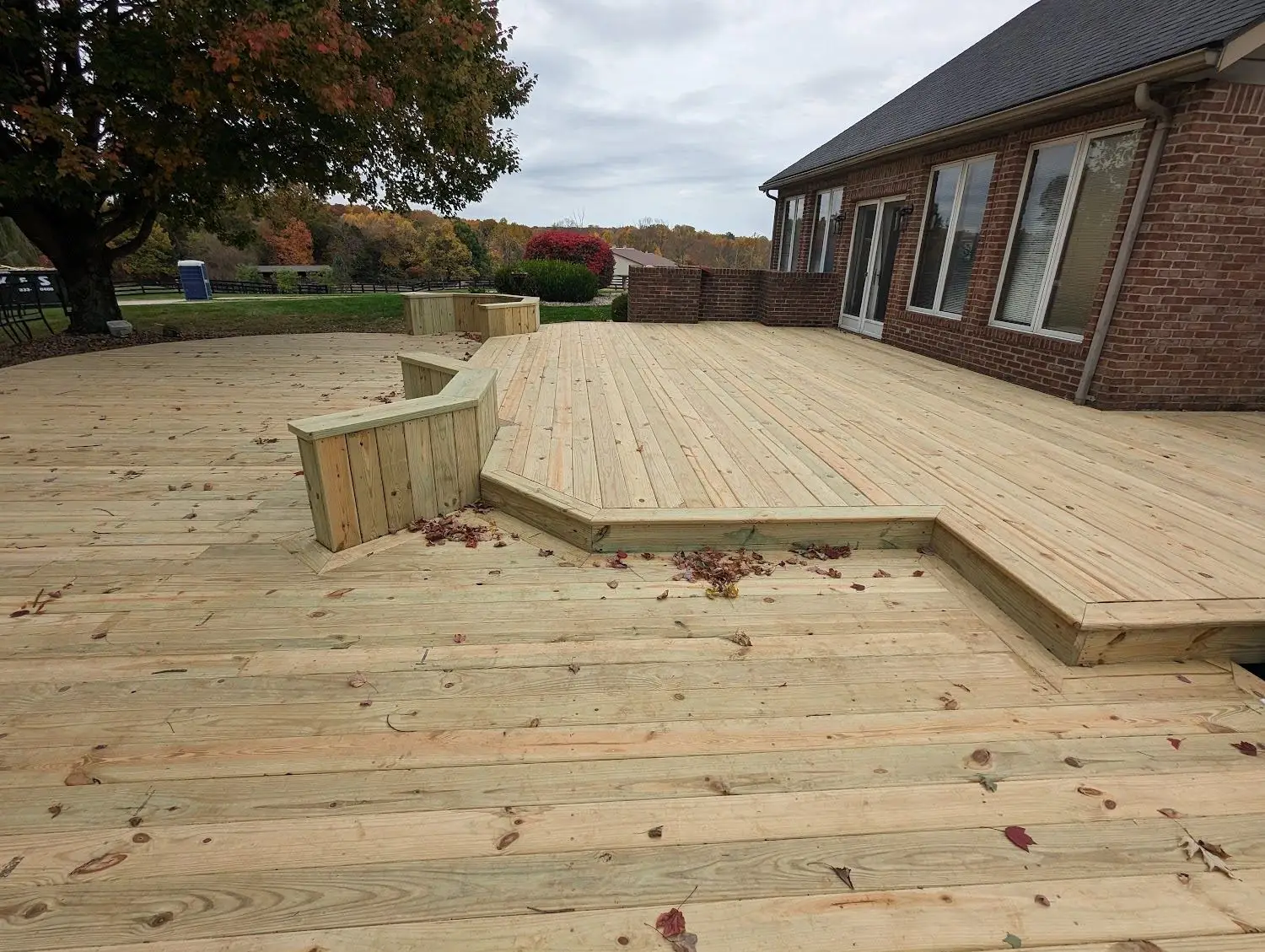 New two-level wood deck with an angled built-in bench seating wall behind a brick home